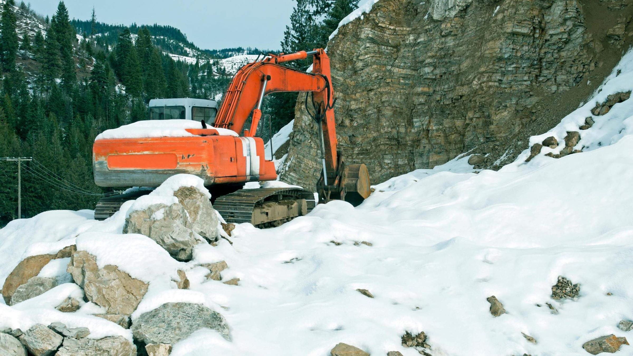 Excavator digging on a snowy mountainside
