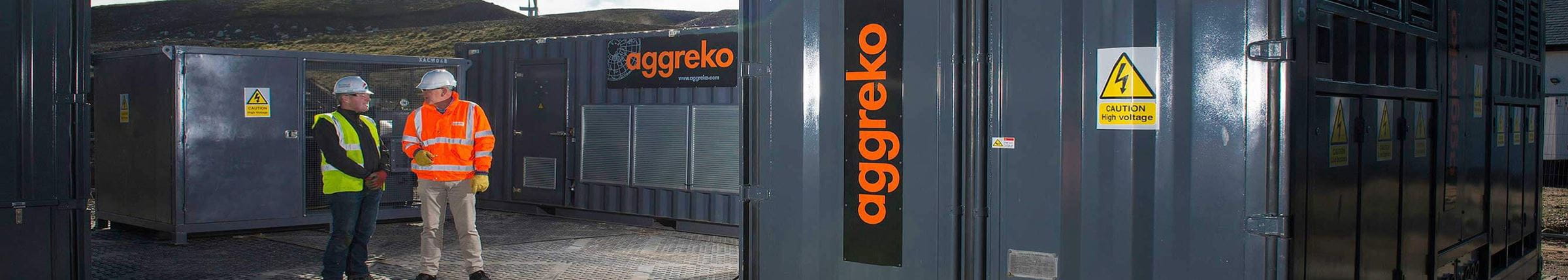 Two engineers standing beside Aggreko equipment in full safety regalia