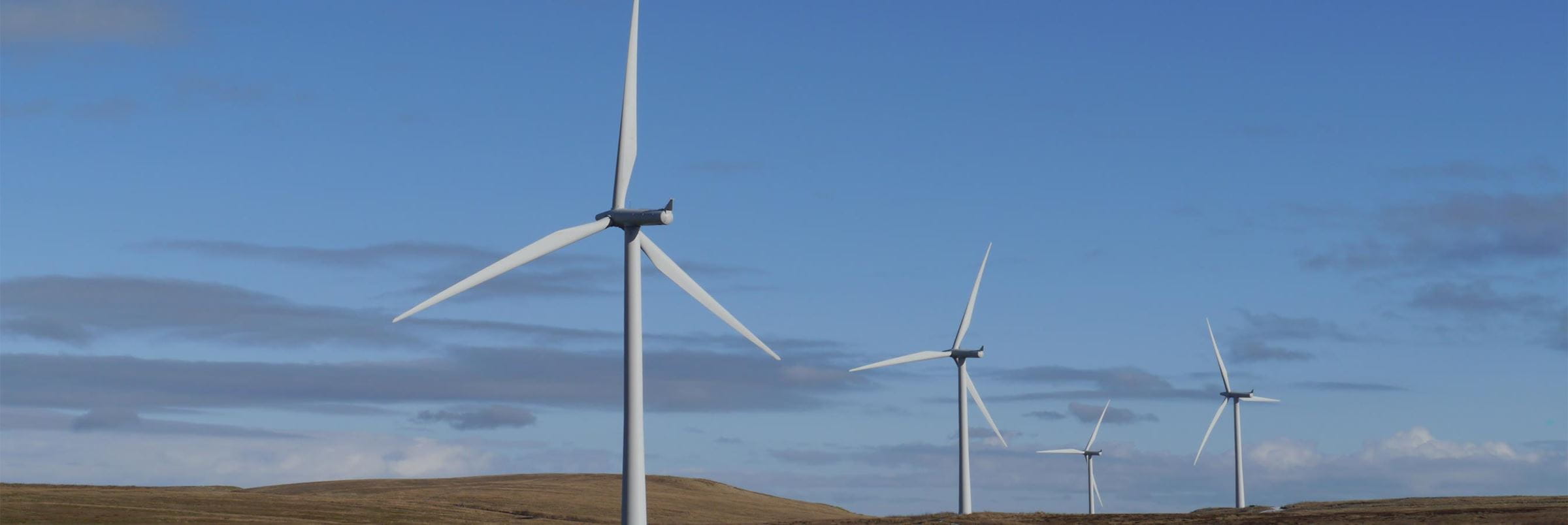 wind turbines situated on grassy hills, with blue sky dotted with clouds in the background