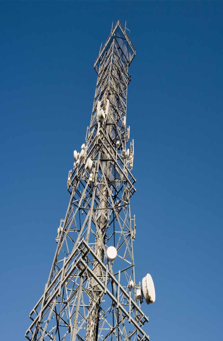 A communications tower with a clear blue sky in the background. The tower is dotted with metal structures and tiny satellite dishes.