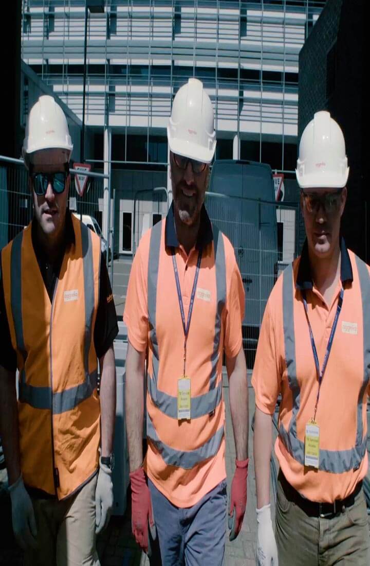 Three technicians wearing orange high visibility jackets and safety helmets and goggles