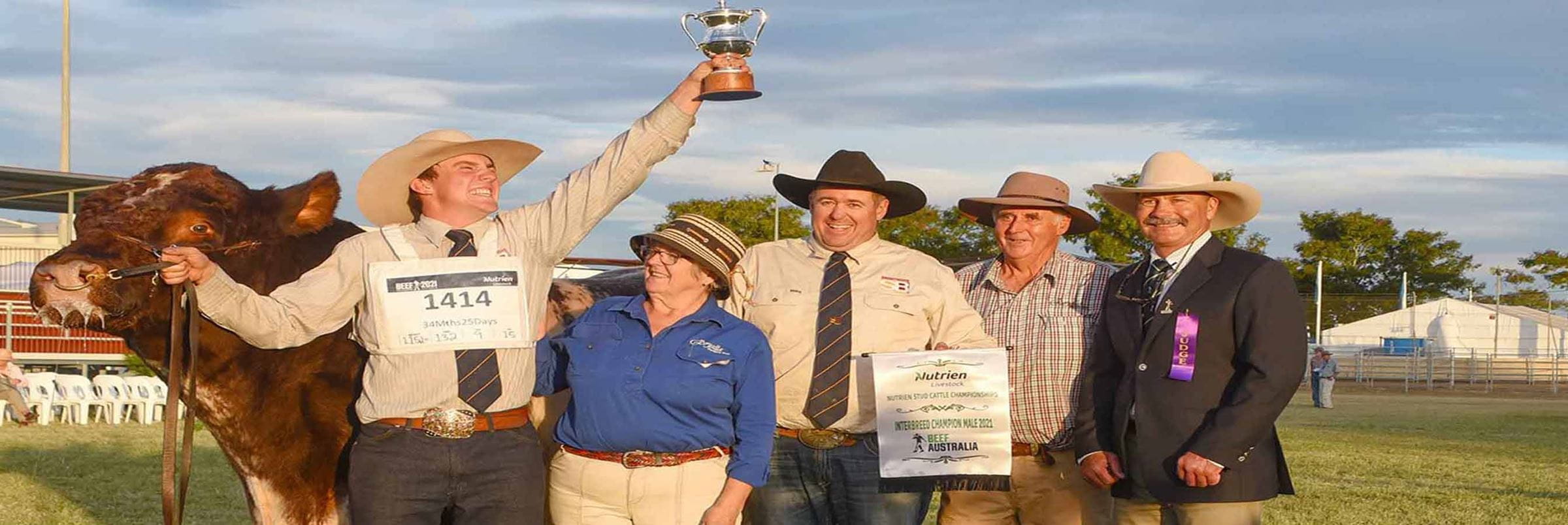 A group of people wearing cowboy hats with a cow and one person lifting  a trophy