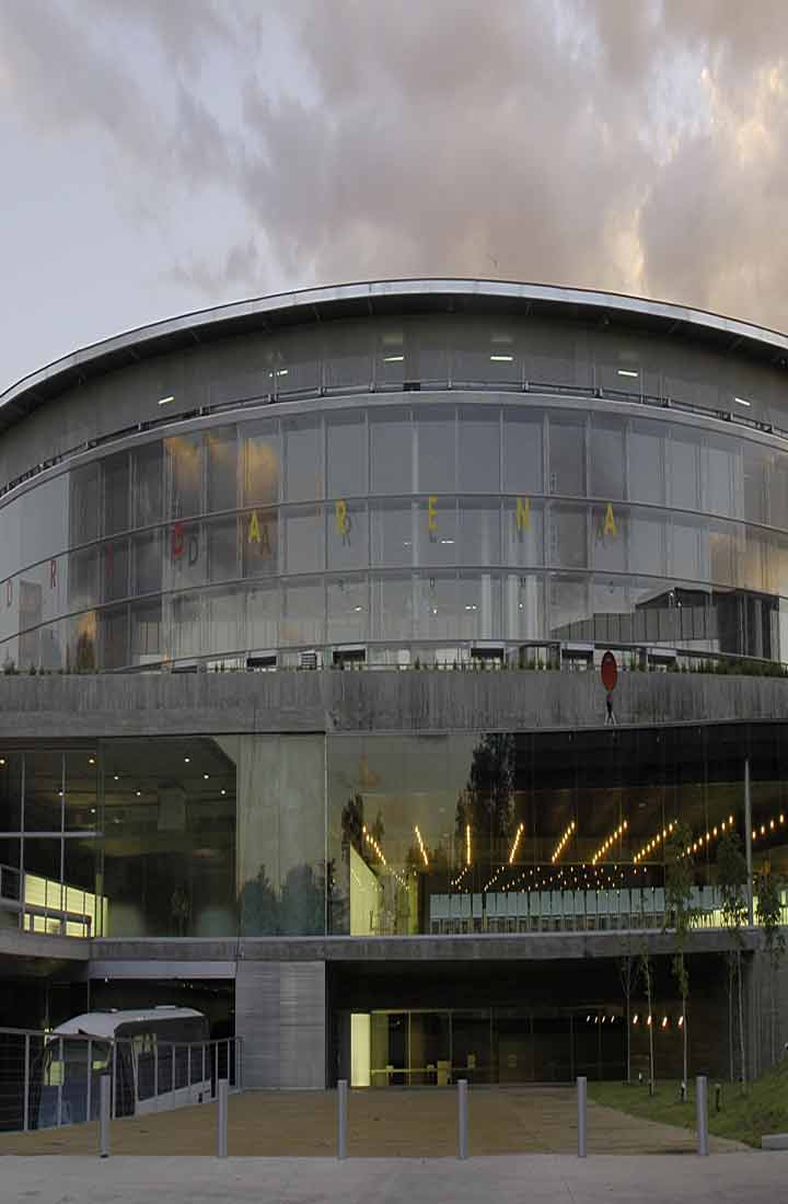 Outside view of the Madrid arena, with cloudy sky as an atmospheric backdrop to an impressive feat of architecture that is moulded by glass, steel and concrete