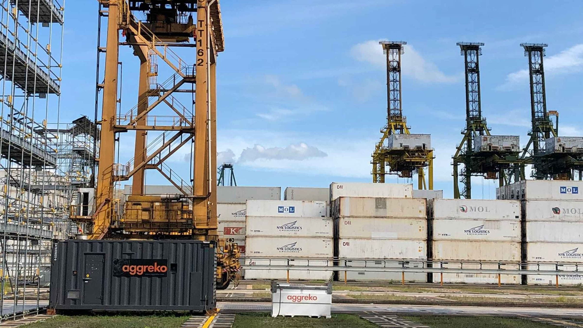 Aggreko generator with containers in the background and a crane at the docks